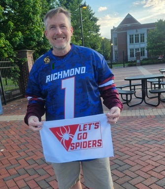 Shawn wearing a Richmond Spiders Jersey and hold a "Lets Go Spiders" towel at a game.
